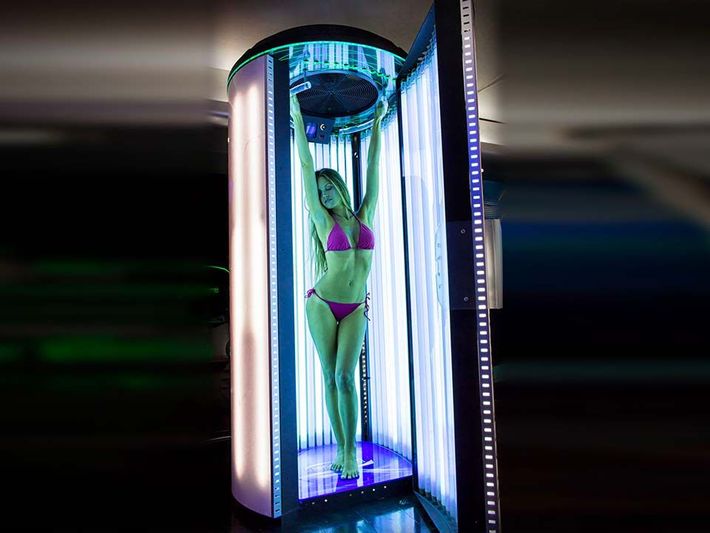 Donna in bikini rosa all'interno di una cabina abbronzante verticale con luci blu e bianche.