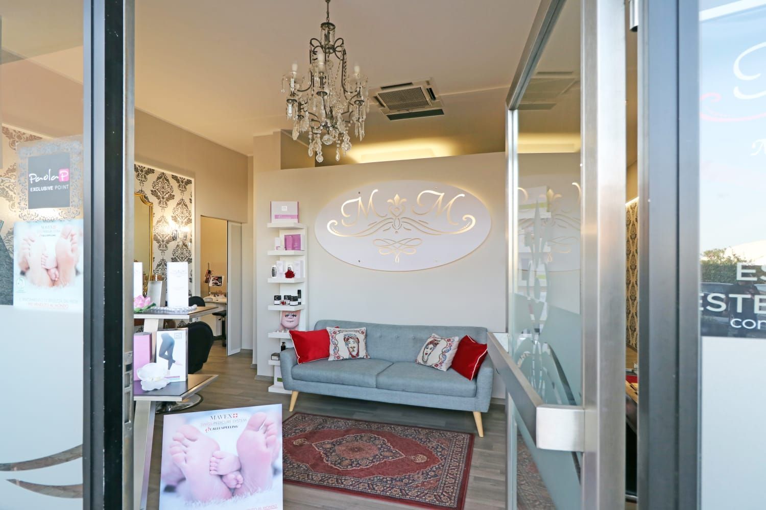 Ingresso del salone con zona d'attesa; divano azzurro, cuscini rossi, lampadario decorato, parete decorativa.