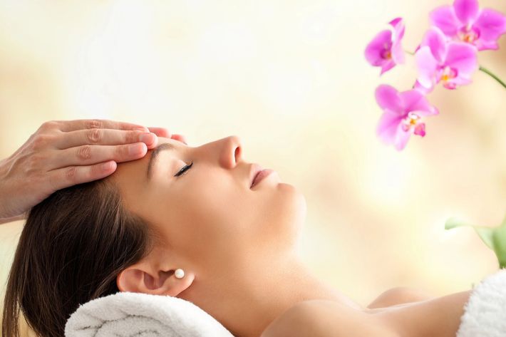 Donna che riceve un massaggio alla testa, occhi chiusi, ambiente spa con orchidee rosa.