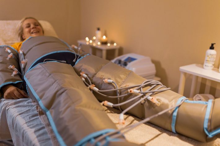 Donna in tuta compressiva, sdraiata su un lettino da massaggio, sorridente. Ambiente spa con candele.