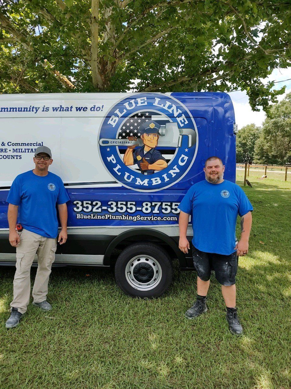 Two men are standing in front of a blue line plumbing truck.