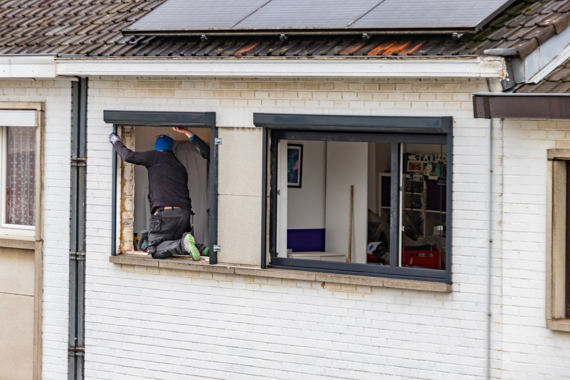 A man is installing a window in a white brick house.