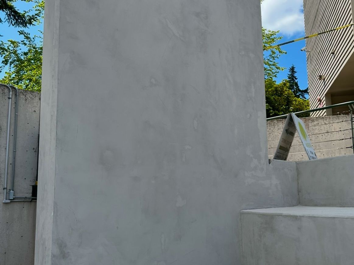 A white wall with a staircase leading up to it and a building in the background.