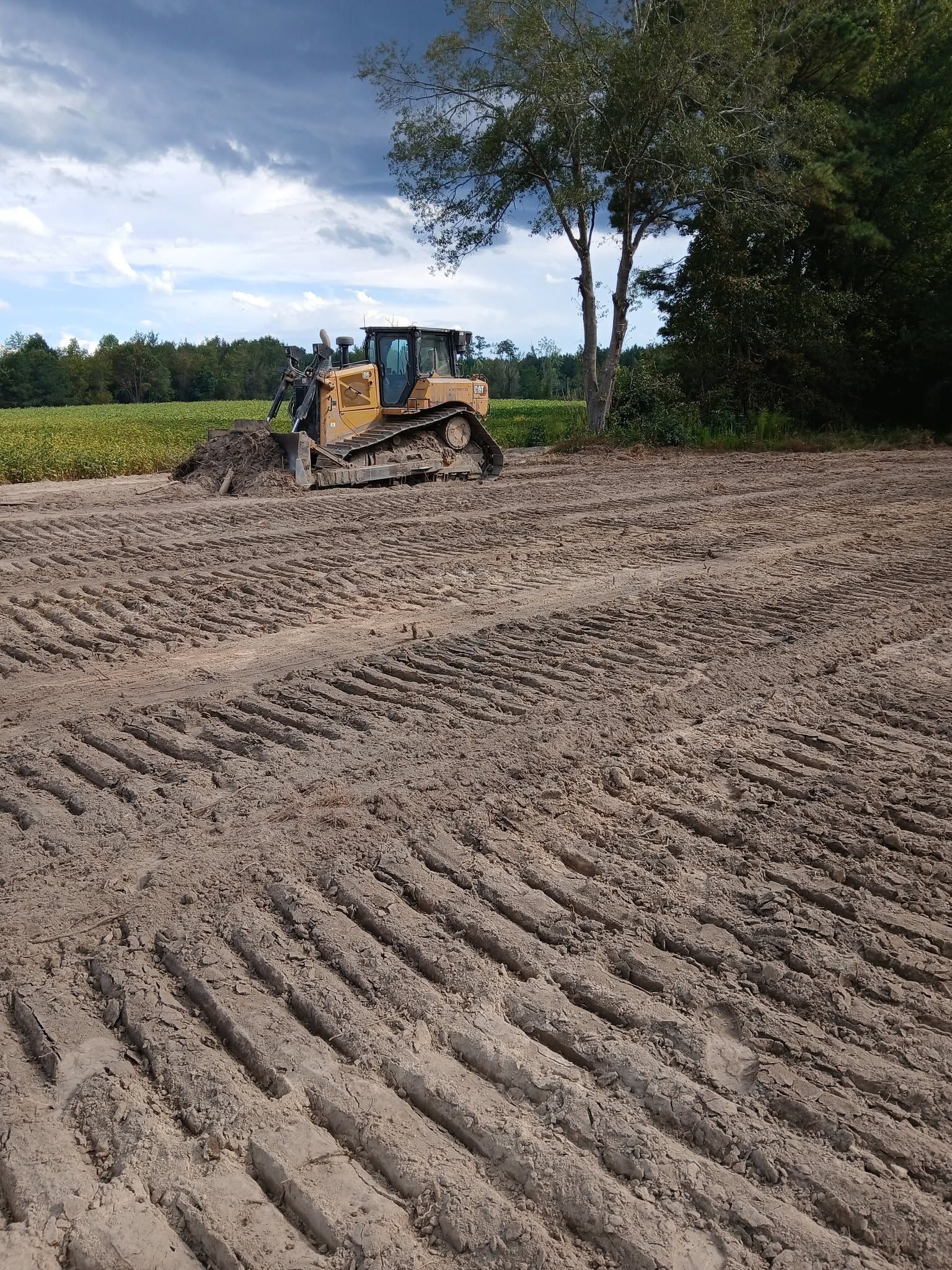 Bulldozer grading a plowed field under a cloudy sky
