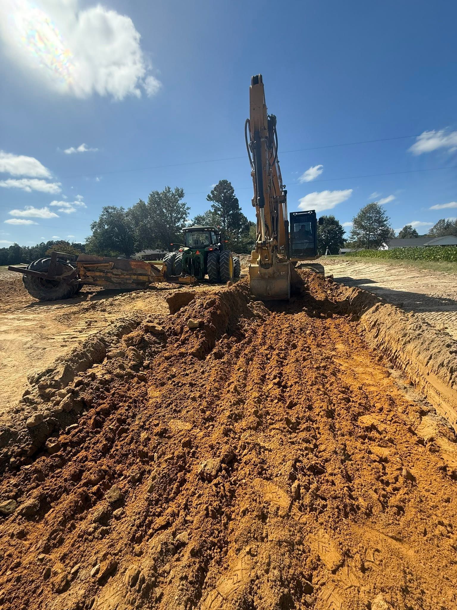 Excavator digging a large dirt mound at a construction site under a clear blue sky.