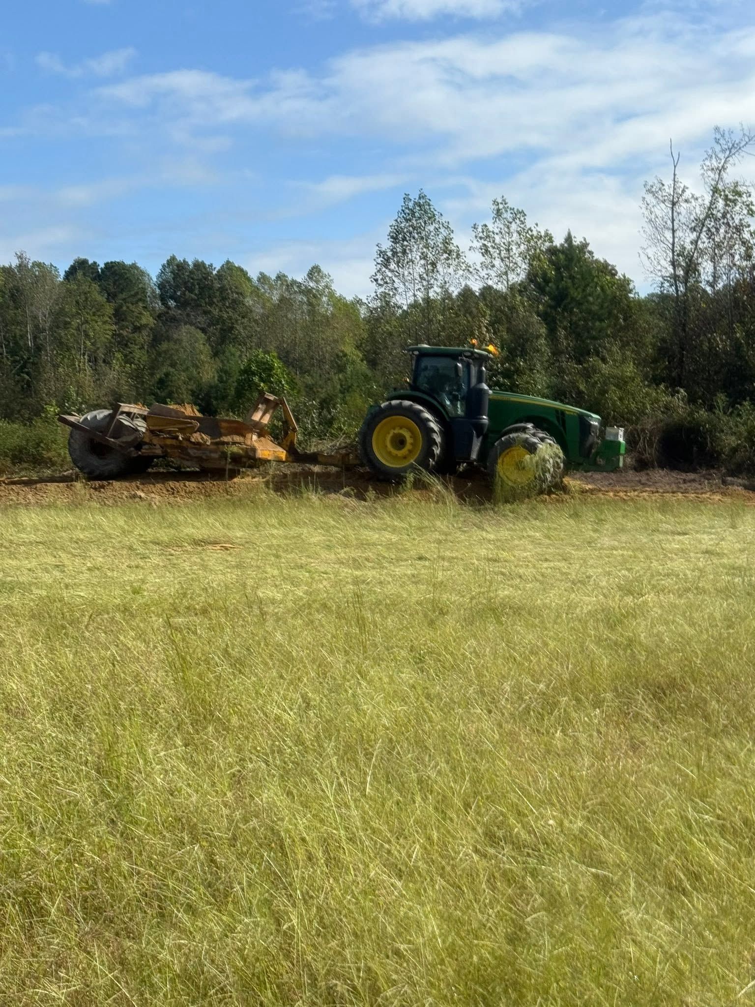 Green tractor hauling logs across a grassy field under a blue sky