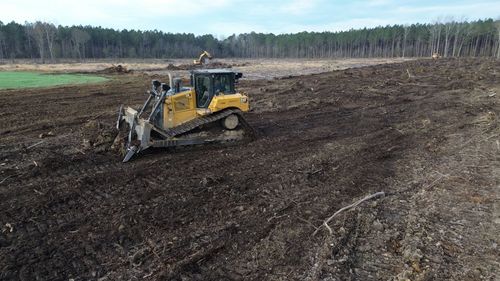Yellow bulldozer clearing a muddy field with a forest line in the background