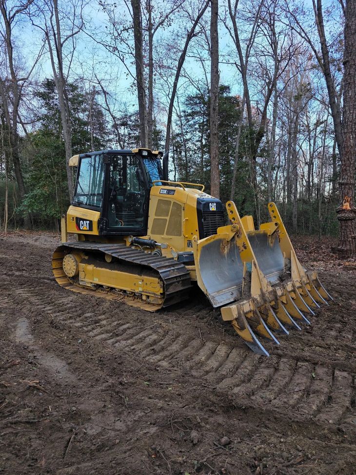Yellow bulldozer with grapple attachment working on a muddy forest trail