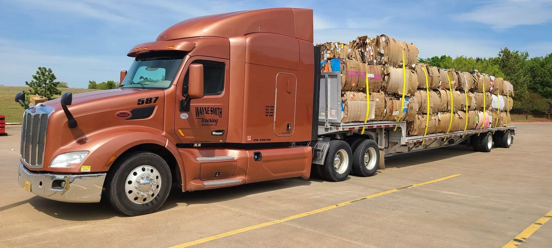 Orange semi-truck hauling a long load of bundled materials in a parking lot