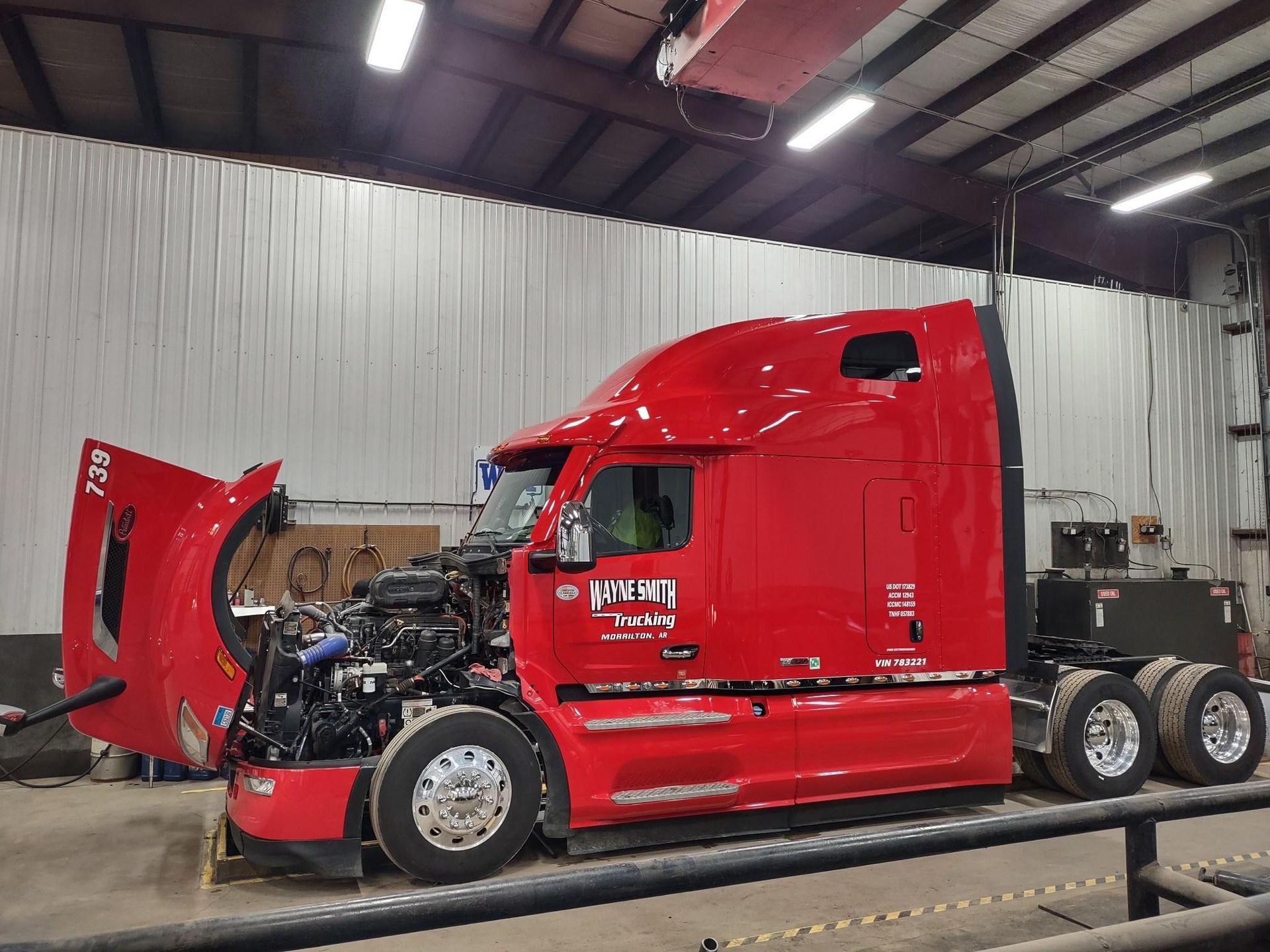 Red semi-truck in a garage with its hood open, exposing the engine.