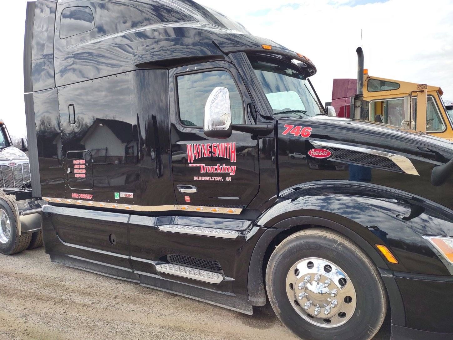 Black semi-truck cab parked on gravel lot with red lettering on the door