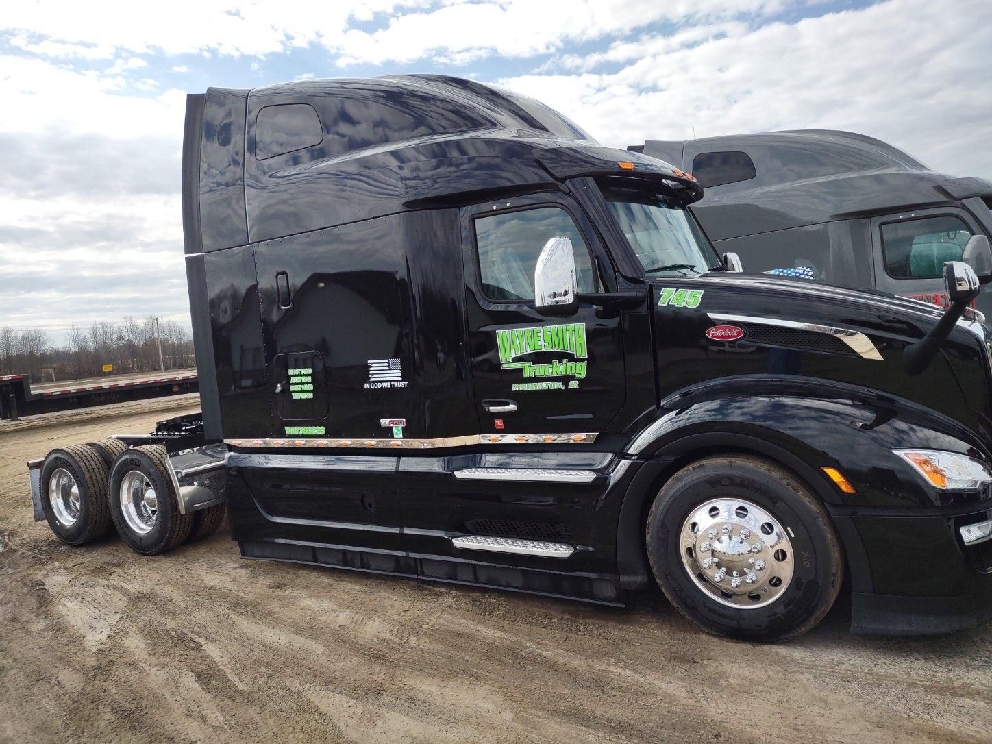 Black semi-truck tractor parked on dirt lot under cloudy sky, side view