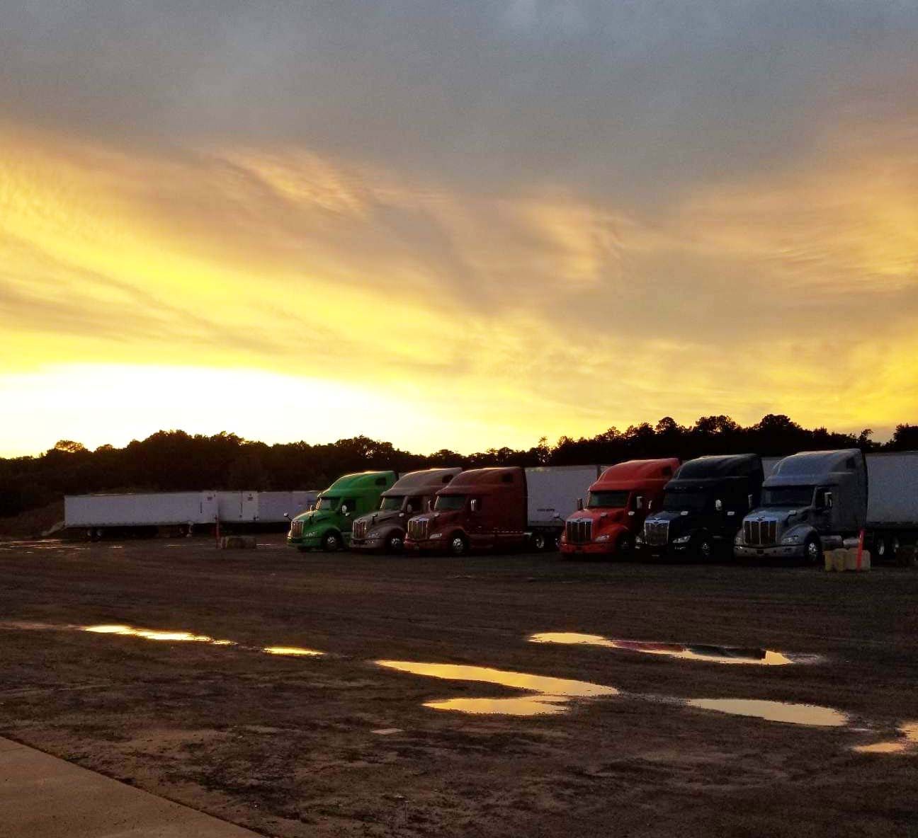 Semi-trucks parked at dusk under a golden sunset sky.