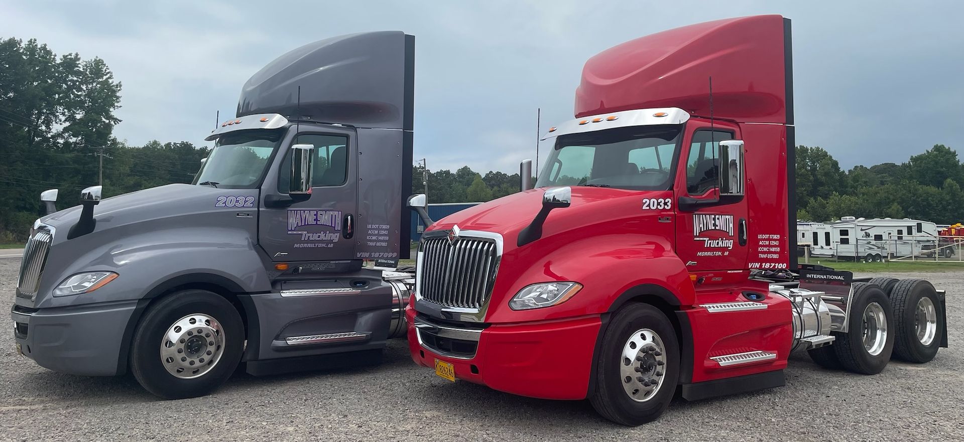 Two semi trucks, one gray and one red, parked side by side outdoors