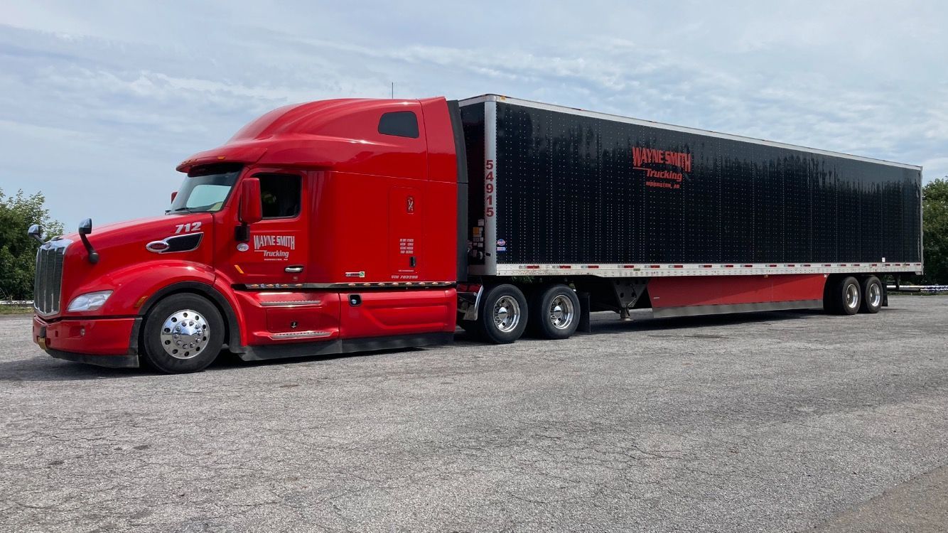 Red semi-truck with black trailer parked on a gravel lot under an overcast sky