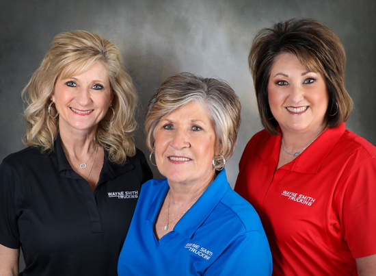 Three smiling employees posing against a gray backdrop, wearing black, blue, and red shirts.