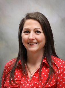 Woman smiling in a red polka-dot blouse against a gray studio backdrop