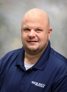 Portrait of a smiling man in a navy polo shirt against a blurred studio background