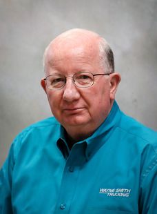 Portrait of a man in a teal button-up shirt and glasses against a gray studio background