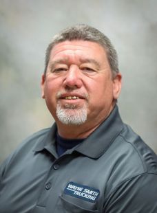 Studio portrait of a man in a gray collared shirt with an embroidered logo, against a neutral background