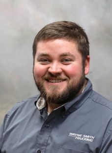 Smiling man with short brown hair and beard in a gray button-up shirt against a plain backdrop