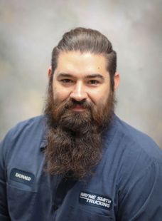 Portrait of a bearded man in a blue shirt against a gray studio backdrop