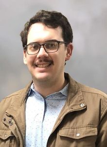 Smiling man in a dark polo shirt against a gray studio backdrop