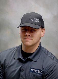 Person in a dark gray uniform and cap against a neutral gray background, looking at the camera.