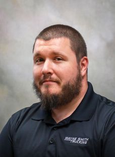 Portrait of a bearded man in a dark polo shirt against a gray studio background