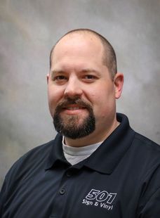 Portrait of a smiling man in a dark polo shirt against a gray studio background