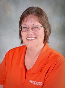 Smiling person in an orange shirt against a gray studio background
