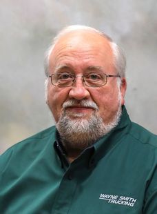 Portrait of a man with glasses and a gray beard wearing a green collared shirt against a neutral background