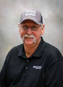 Smiling man in a gray cap and glasses wearing a black polo shirt against a soft studio backdrop