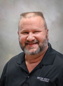Smiling man in a dark polo shirt against a gray studio backdrop