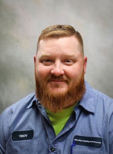 Smiling man with red beard in blue shirt and green undershirt against a gray backdrop