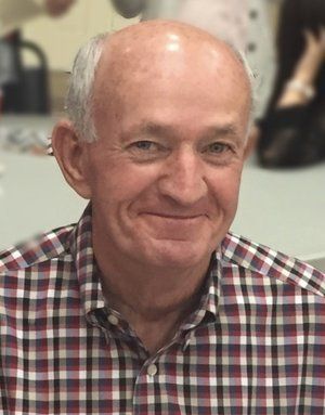 Smiling man in a red-and-white plaid shirt against a blurred indoor background