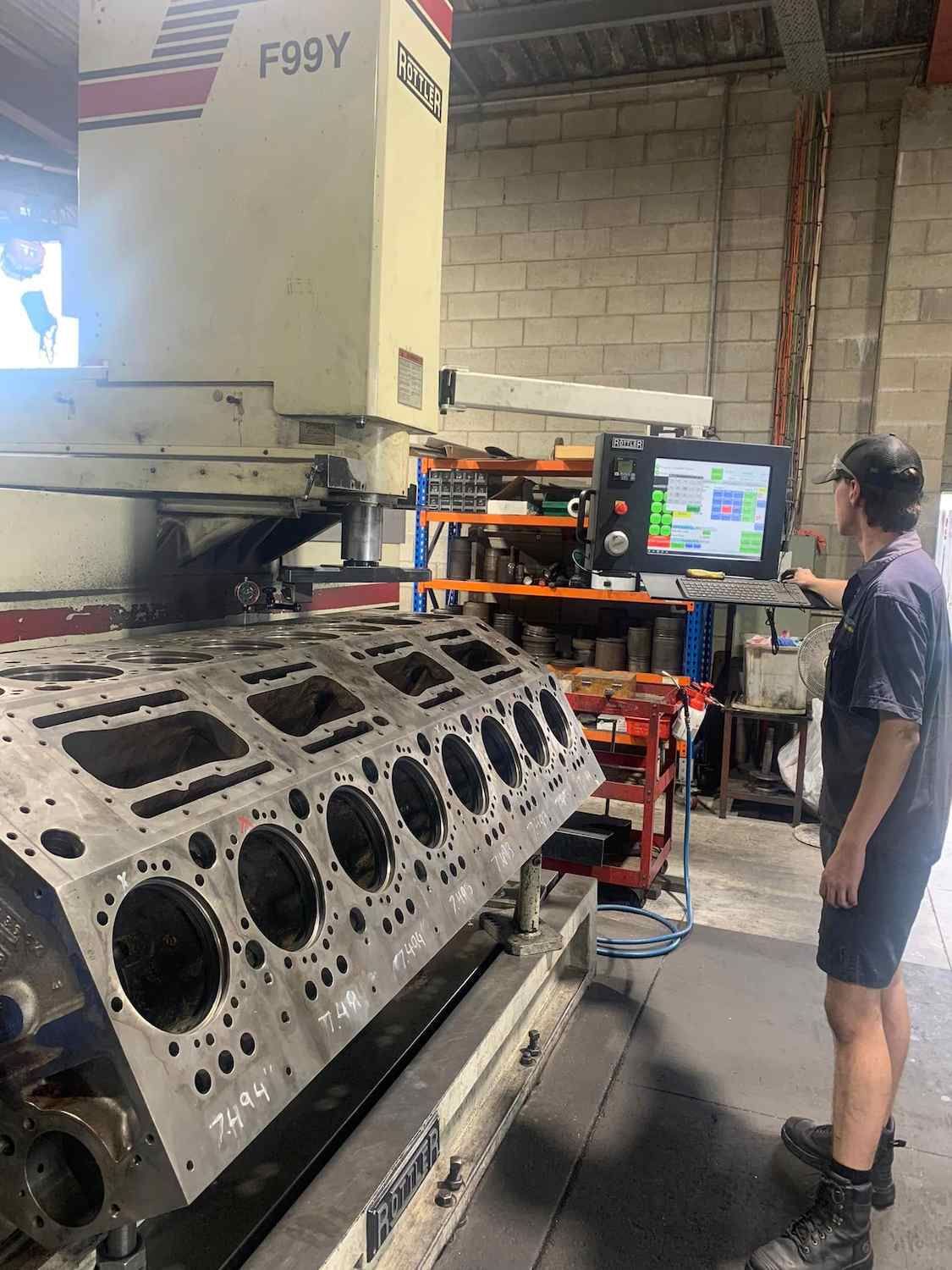 A Man is Standing in Front of a Machine in a Garage — Curtin Engine Reconditioning Pty Ltd In Paget, QLD