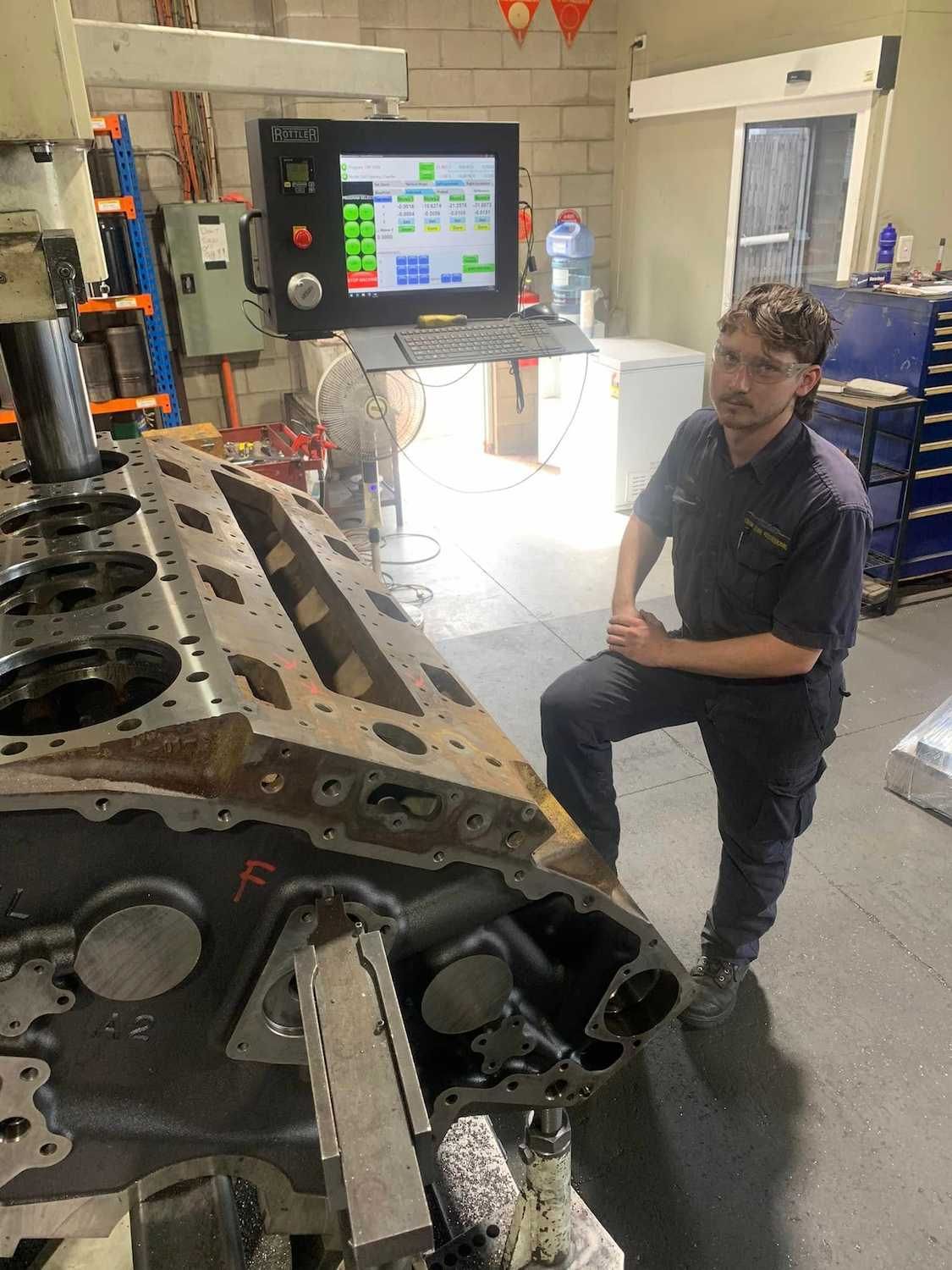 A Man is Kneeling Down in Front of a Machine in a Garage — Curtin Engine Reconditioning Pty Ltd In Paget, QLD
