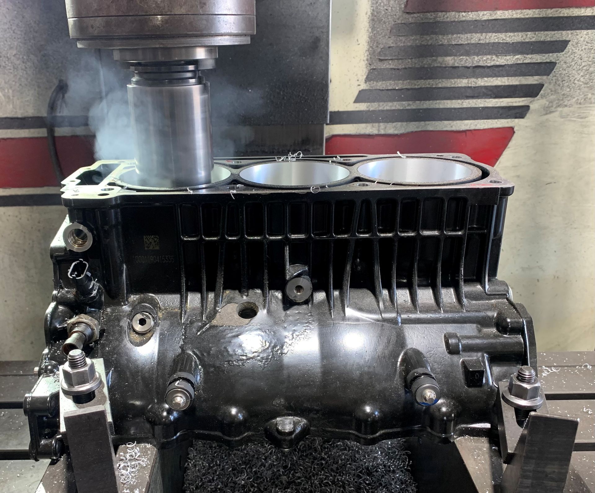 A black engine block is being milled by a machine, producing smoke and metal shavings.— Curtin Engine Reconditioning Pty Ltd In Paget, QLD