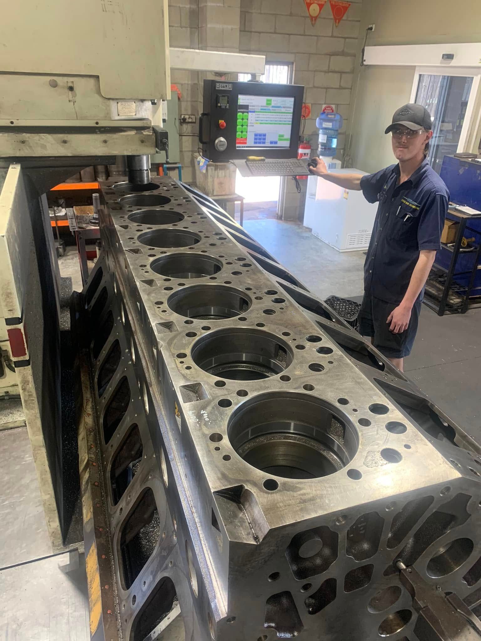 A person operates machinery, working on a large engine block in a workshop.  Curtin Engine Reconditioning Pty Ltd In Paget, QLD