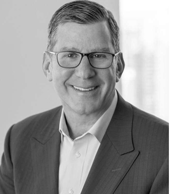 A man in a suit and glasses is smiling in a black and white photo.