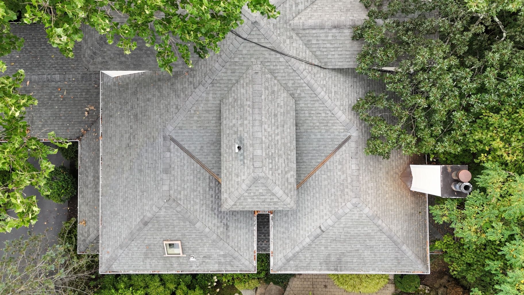Overhead view of a house with a gray shingled roof, trees, and a chimney.
