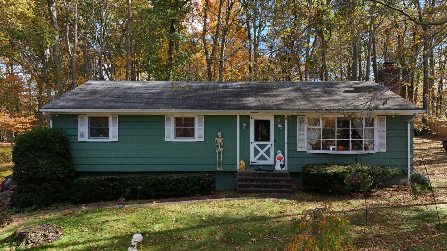 Green house with white trim, set in a yard with fall foliage and a brick chimney.