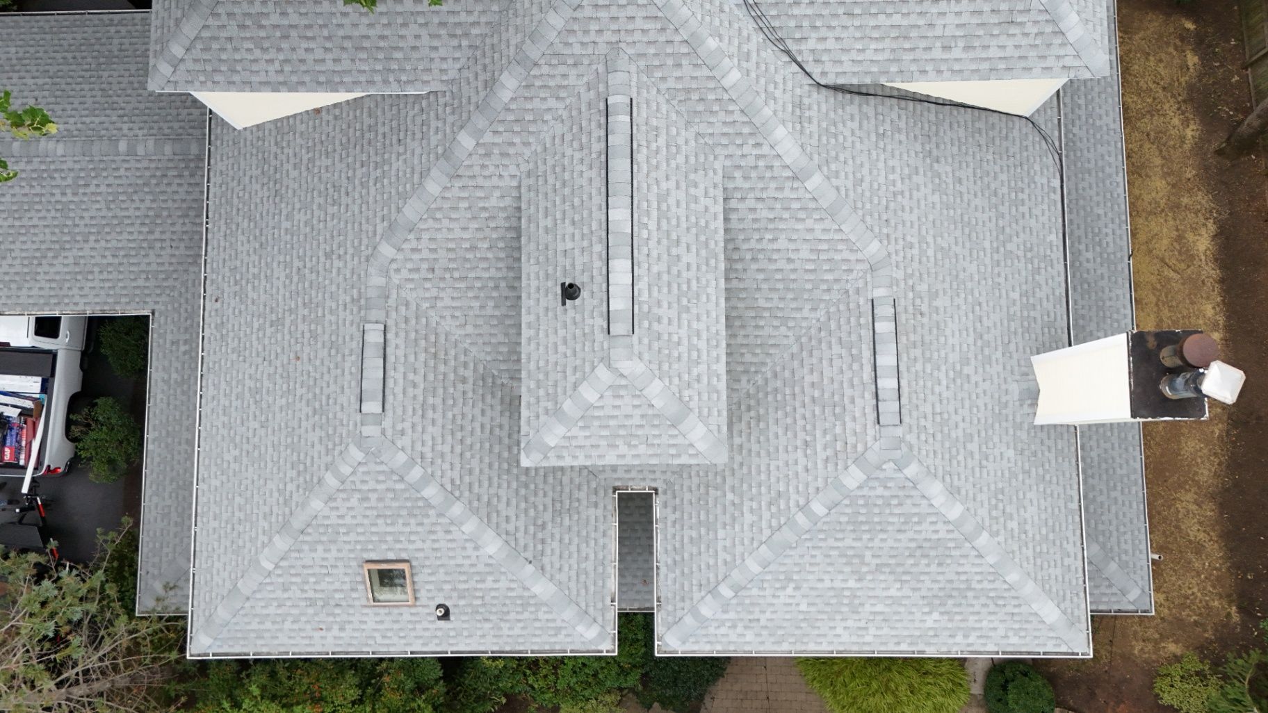 Overhead view of a house with a gray shingled roof, trees, and a vehicle parked in the driveway.