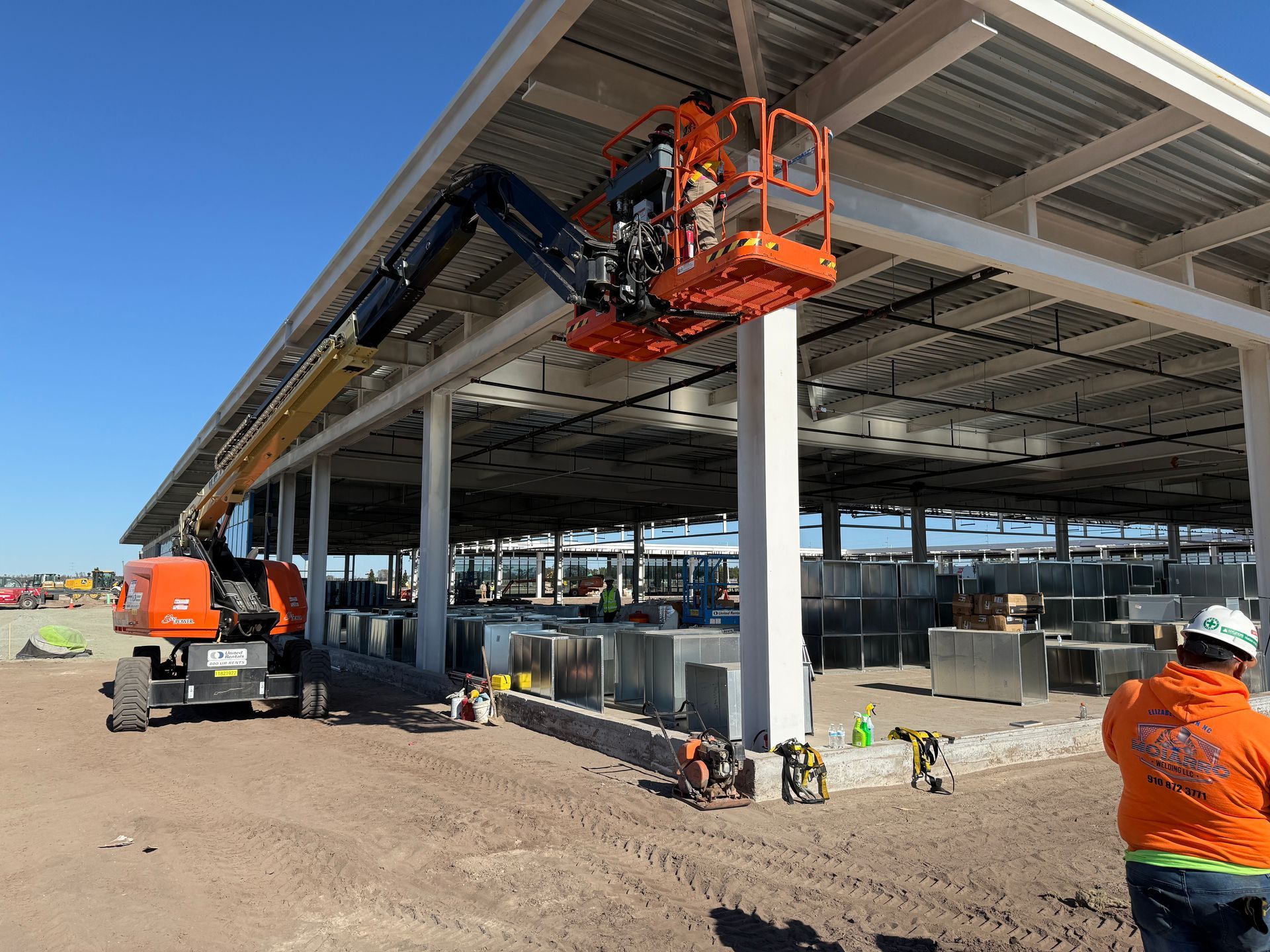 A man in an orange shirt is standing in front of a construction site