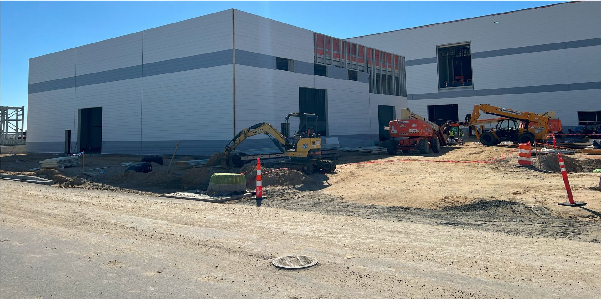 A large white building is being built next to a dirt road.