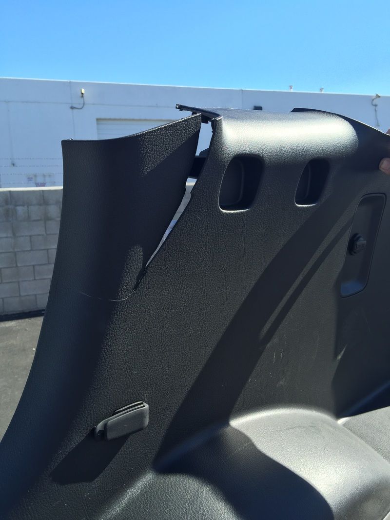 Black car interior panel with two headrest openings, outdoors against a blue sky and concrete wall.