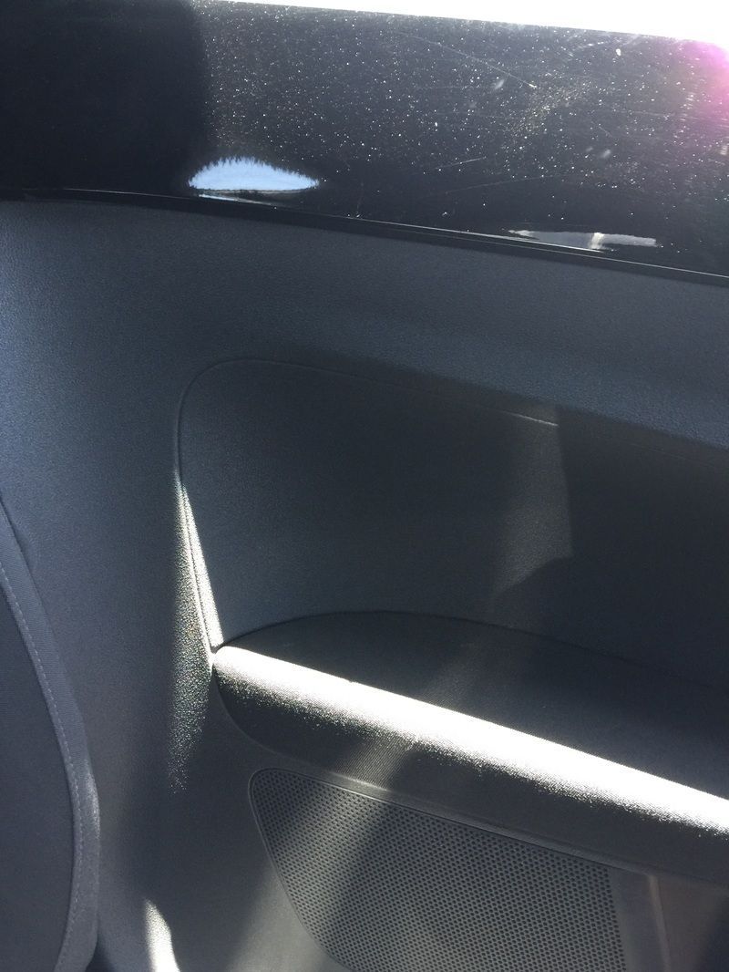 Close-up of a dark car interior door handle with textured panel and light glare on the window.