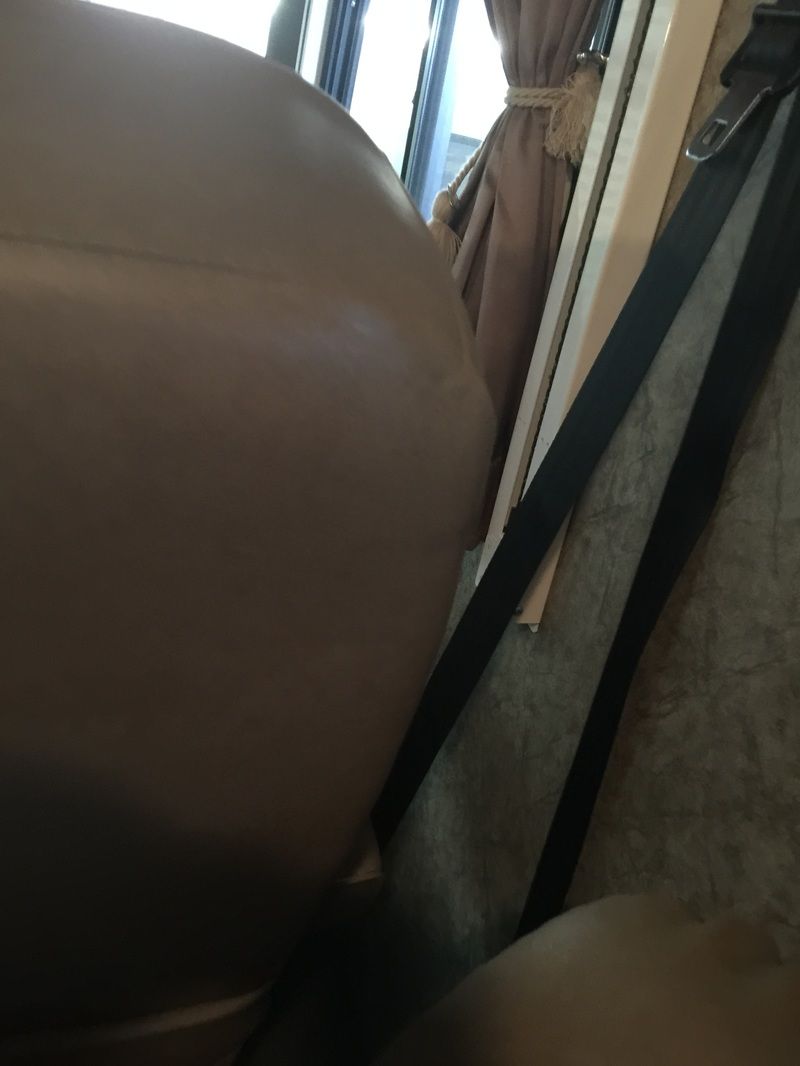 Close-up of a brown leather seat beside a window with curtains and a black strap.