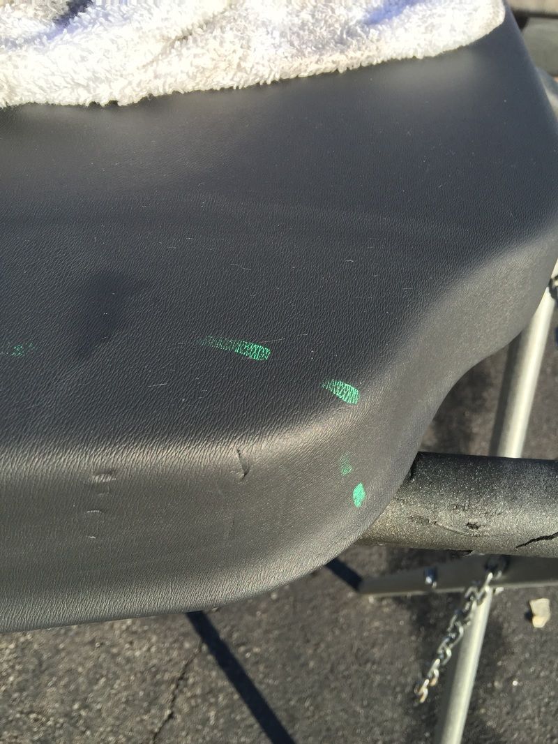 Close-up of a black textured chair seat with green paint marks and a metal frame.